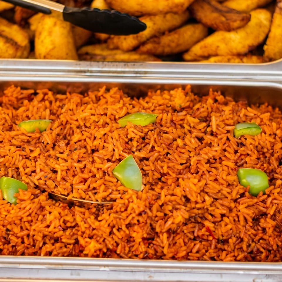 Tray of orange seasoned rice garnished with green peppers, with fried plantains in the dish above.