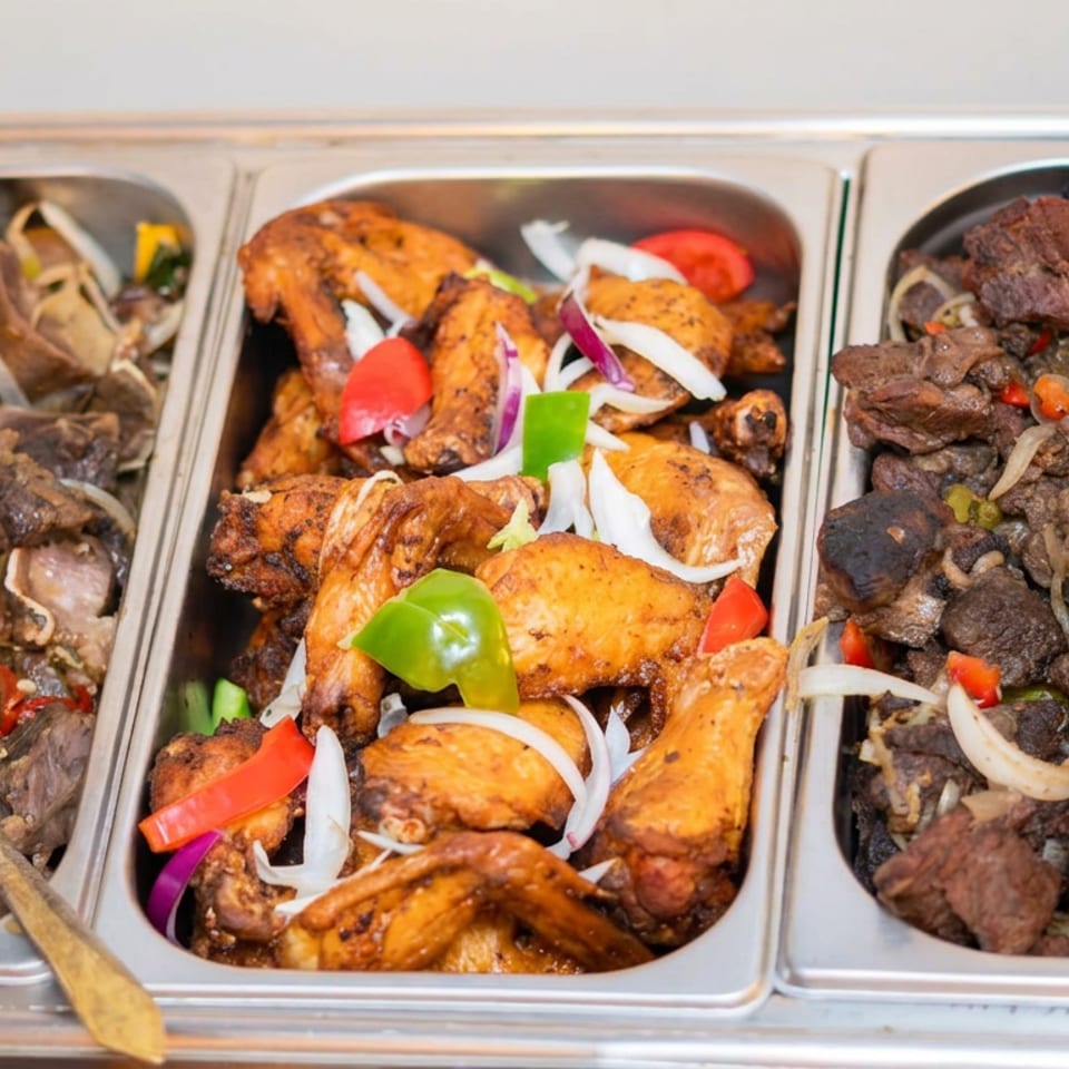 Three stainless-steel buffet trays hold seasoned meat, roasted chicken, onions, and colorful peppers.