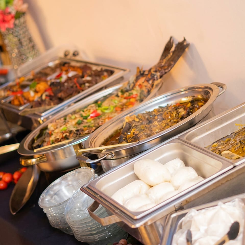 Buffet table displaying assorted cooked dishes, seafood, dumplings, fried items, and vegetables, with a person photographing the spread.